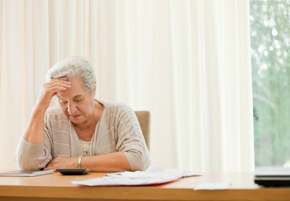 Woman sits at a desk looking at a calculator and rubbing her head.