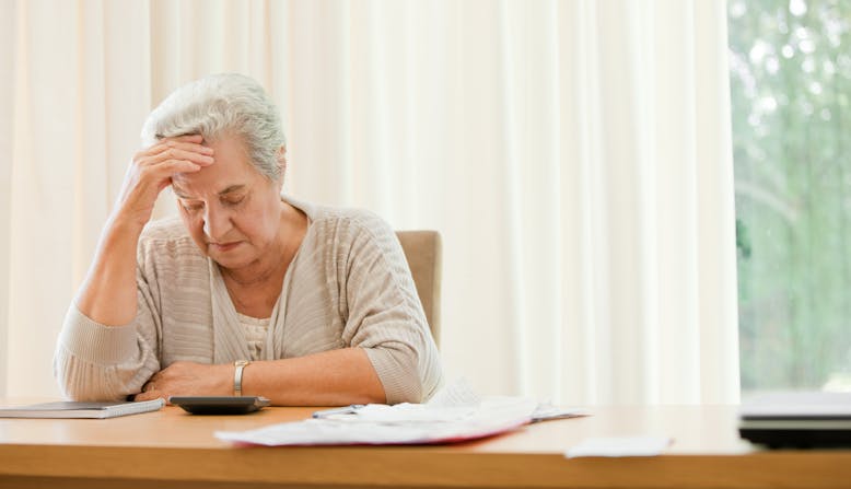 Woman sits at a desk looking at a calculator and rubbing her head.
