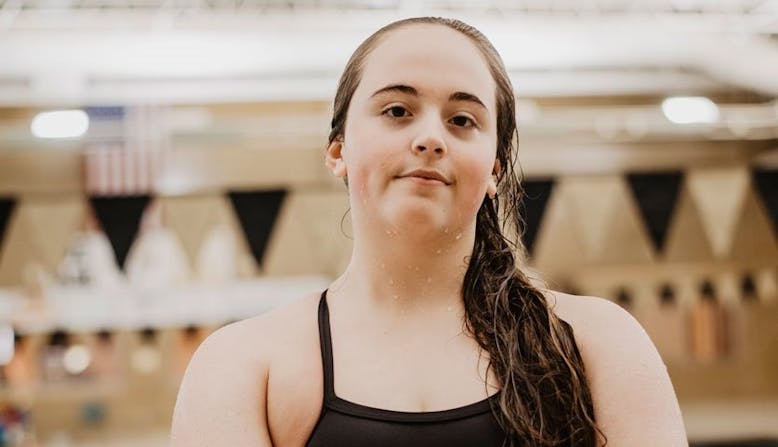 Lena Oslund stands proud at a swimming pool, in a bathing suit and wet from the water.