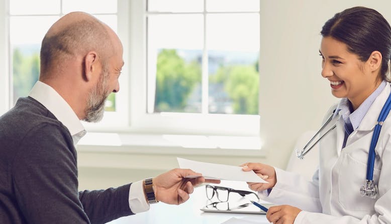 Woman doctor of color handing a prescription note to an older male patient.