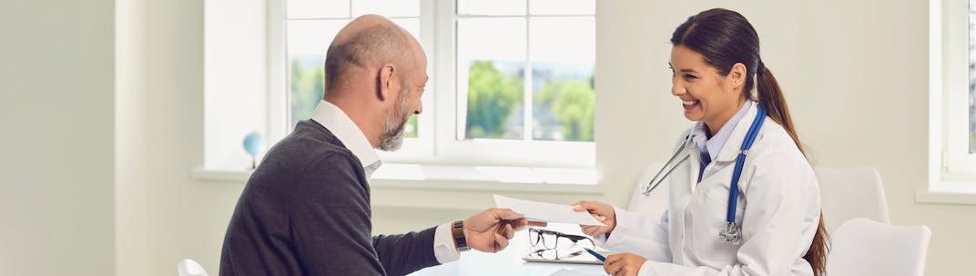 Woman doctor of color handing a prescription note to an older male patient.