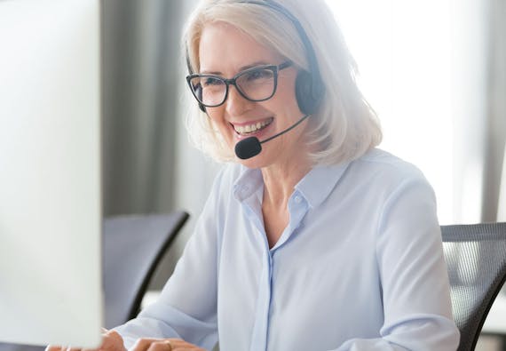 A woman sitting at a computer and wearing a headset smiles. 