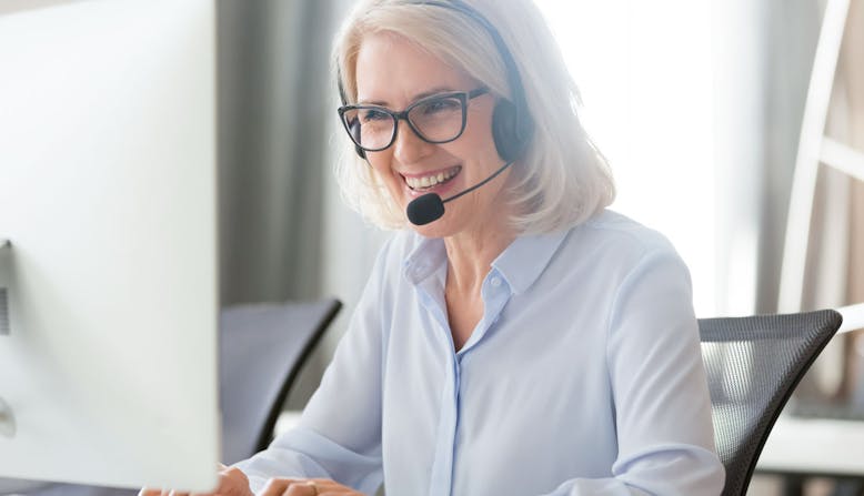 A woman sitting at a computer and wearing a headset smiles.
