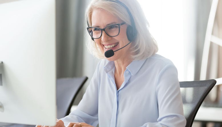 A woman sitting at a computer and wearing a headset smiles. 