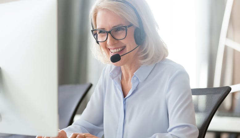 A woman sitting at a computer and wearing a headset smiles.