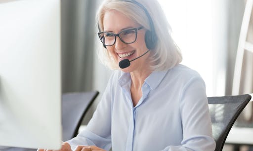A woman sitting at a computer and wearing a headset smiles.