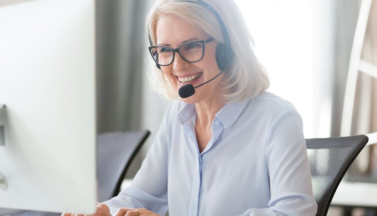 A woman sitting at a computer and wearing a headset smiles.
