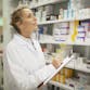 A pharmacist smiles while looking at treatments and confirming stock levels.