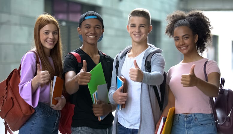 A group of young teens smiling and giving thumbs-up.