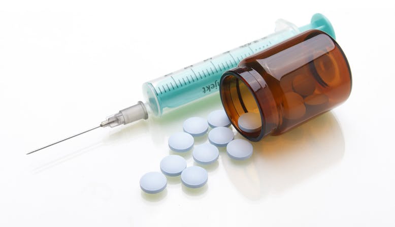 A syringe and a bottle of pills laying on its side with pill spilling out