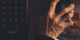 A hand using a computer mouse next to a keyboard.