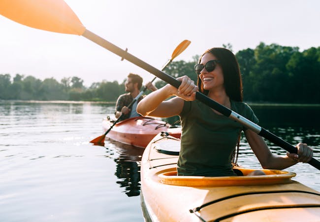 A couple kayak on a lake smiling in the summer.