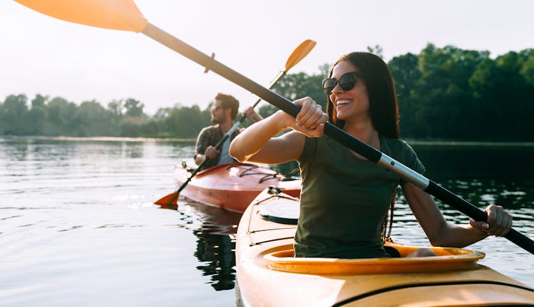 A couple kayak on a lake smiling in the summer.