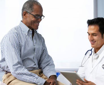 A man sits with his doctor smiling.