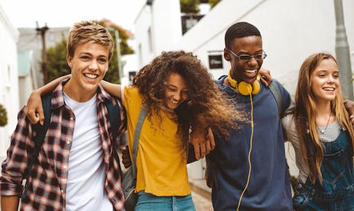 Four teens walking with their arms around each other and smiling.