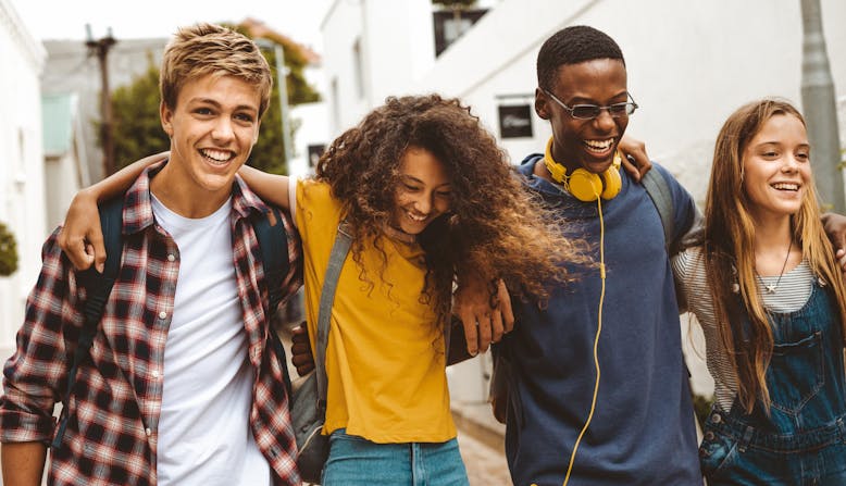 Four teens walking with their arms around each other and smiling.
