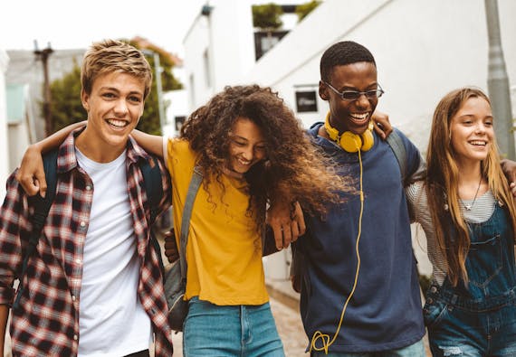 Four teens walking with their arms around each other and smiling.
