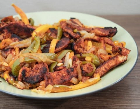 Chicken with onions and peppers on a white plate.