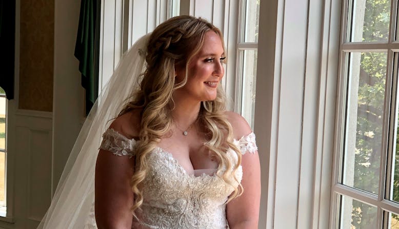 Victoria Ridge in her wedding gown looks out a window.