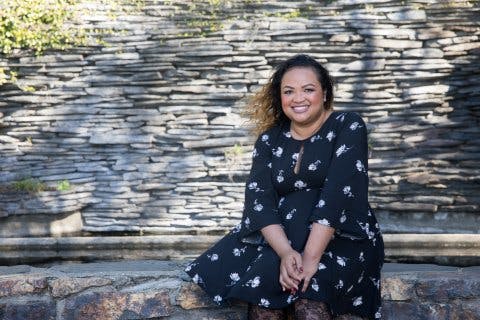Brenda, a psoriasis patient, seated outside in front of a rock wall.