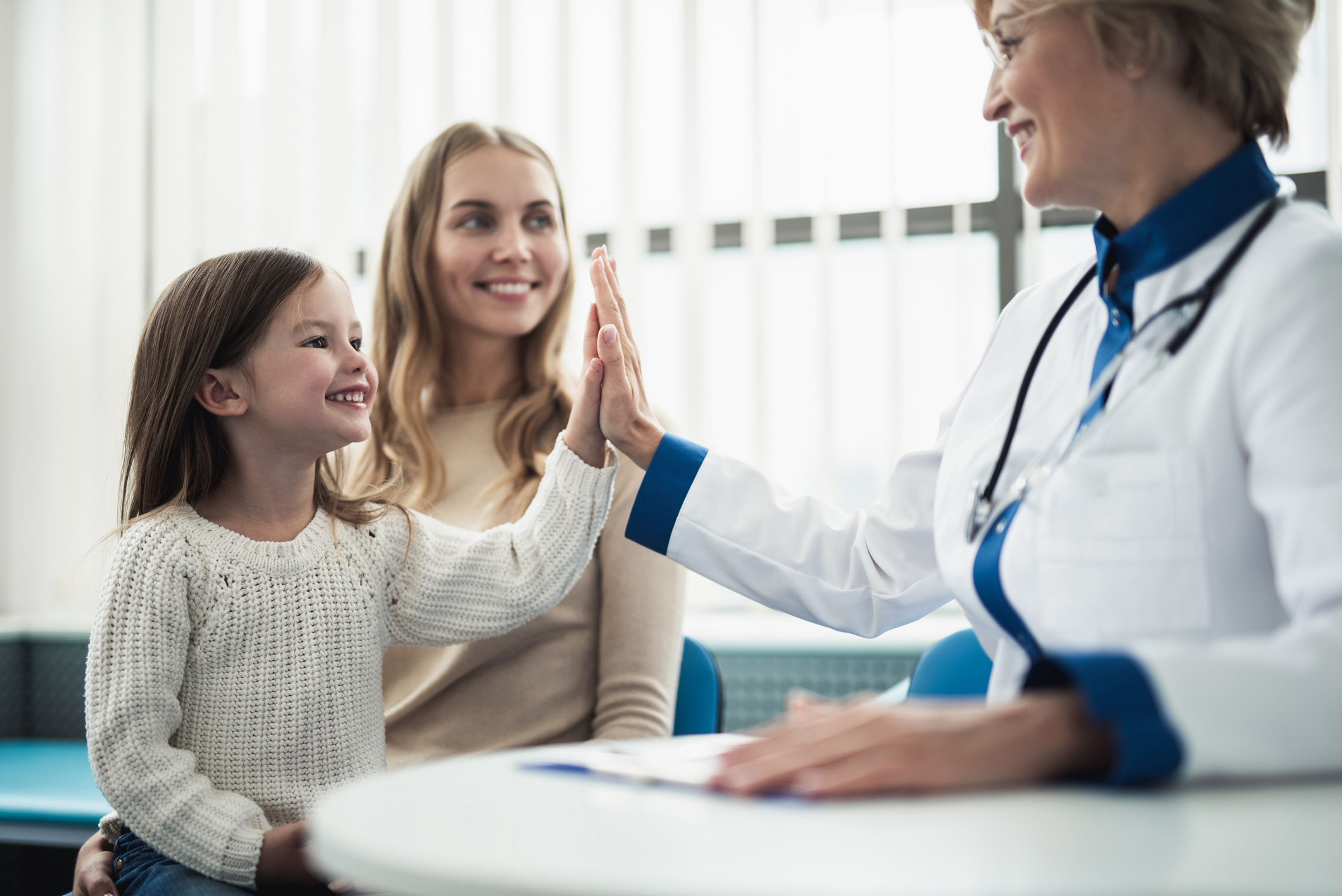 A doctor high-fiving a little girl, while a woman looks on. Everyone is smiling.