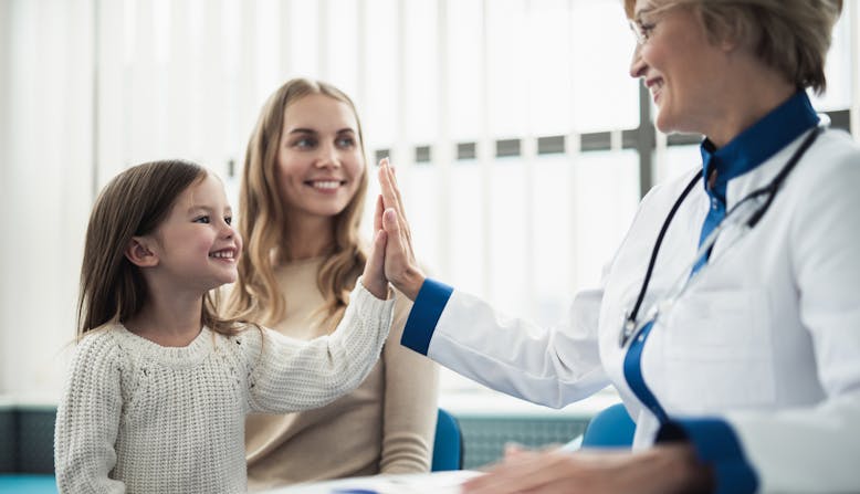A doctor high-fiving a little girl, while a woman looks on. Everyone is smiling.