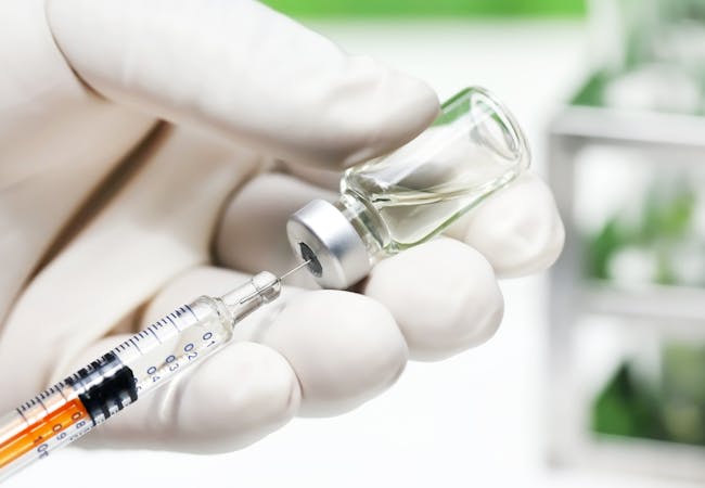 A gloved hand holding a syringe and a vial of medication.