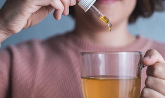 Image of a woman holding a dropper over a cup of tea.