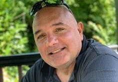 Todd Bello sitting outside and smiling.