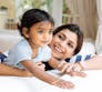A mom and daughter sit on a couch and smile in a living room.