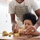 A father and young son knead dough together in their the kitchen.