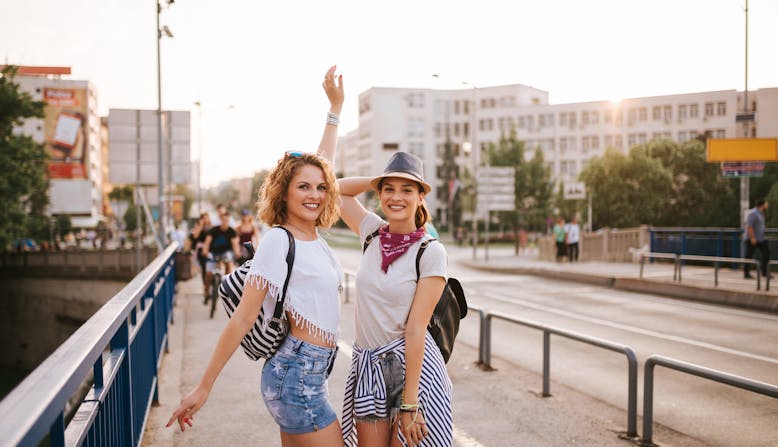 Two women smile and pose on a sidewalk at sunset.