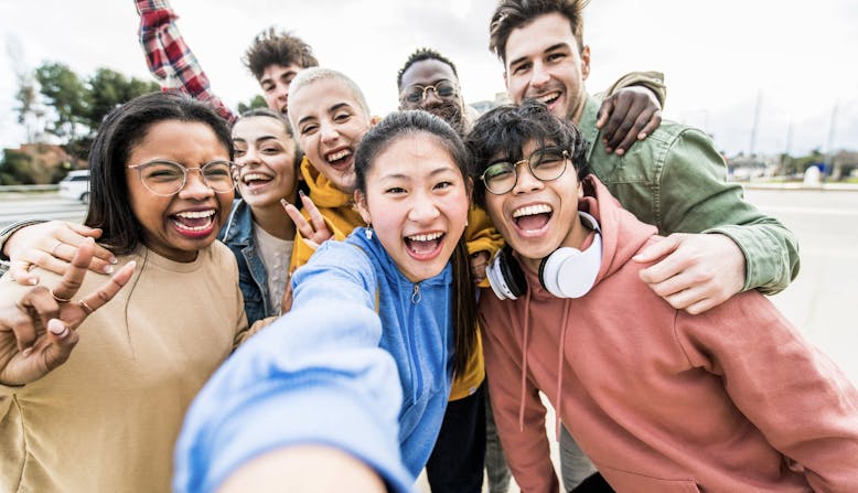 A group of smiling teens take a selfie outside.