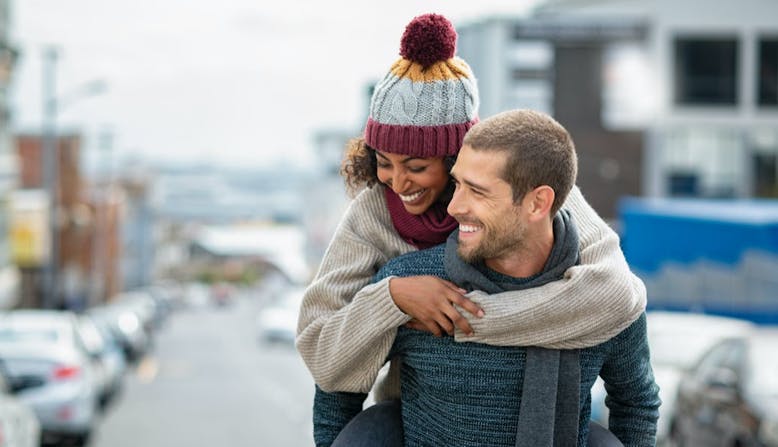 A man gives a woman a piggyback ride, while both are wearing winter clothing. 