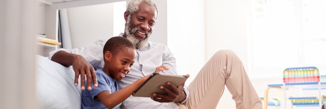 A grandfather sitting with his grandson in a bedroom using digital Tablet together.