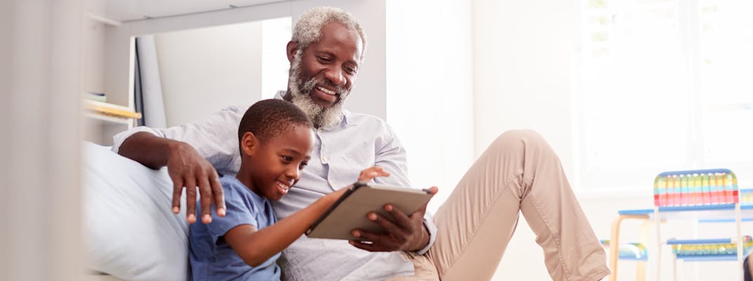 A grandfather sitting with his grandson in a bedroom using digital Tablet together.