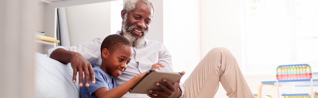 A grandfather sitting with his grandson in a bedroom using digital Tablet together.