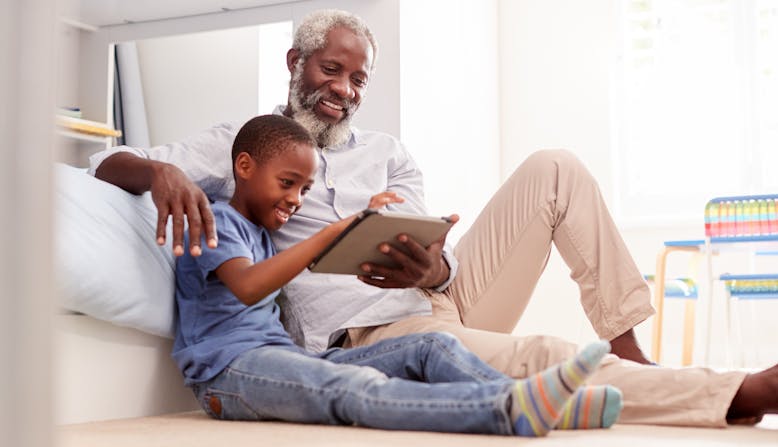 A grandfather sitting with his grandson in a bedroom using digital Tablet together.