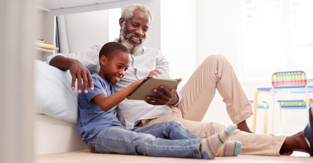 A grandfather sitting with his grandson in a bedroom using digital Tablet together.