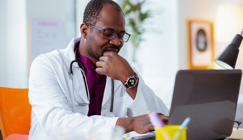 A doctor sits in front of a laptop. 