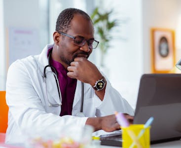A doctor sits in front of a laptop.