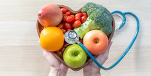 A heart shaped bowl filled with fruits and vegetables with a stethoscope on top.