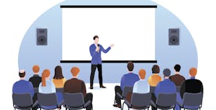 A man in a suit presents to a large group of people seated in chairs.