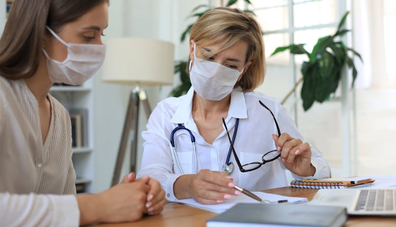 A woman doctor and a woman patient looking at documents at a desk.