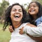 A mother holding her daughter on her back, both laughing