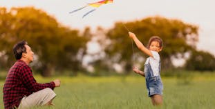 A father and daughter flying a kite in a park.