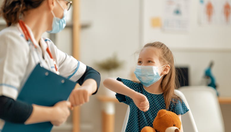 A doctor and child patient bump elbows and smile in a clinic.