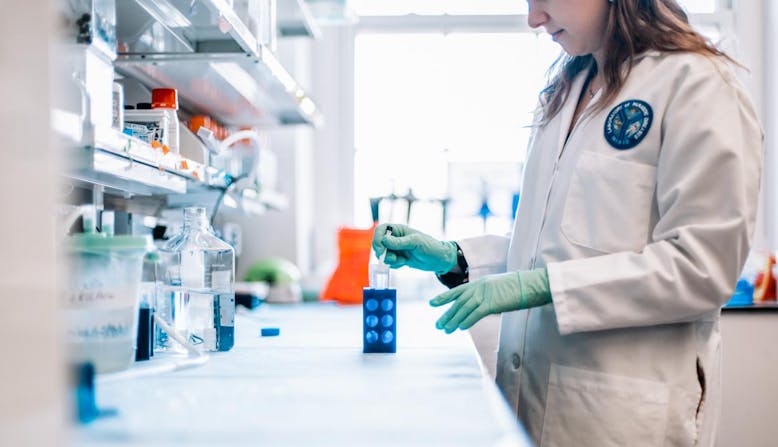 A female researcher  works in a lab with a dropper and container.
