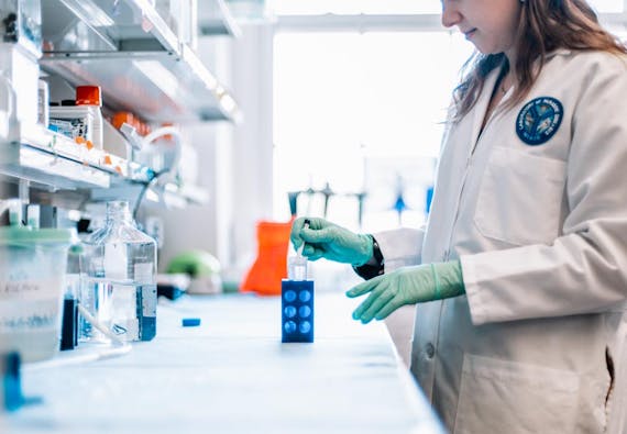 A female researcher  works in a lab with a dropper and container.