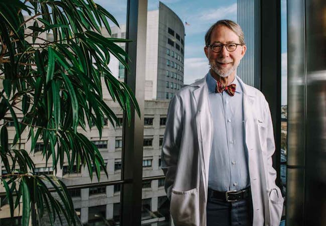 Doctor Philip Mease poses and smiles while wearing a bow tie and lab coat. 